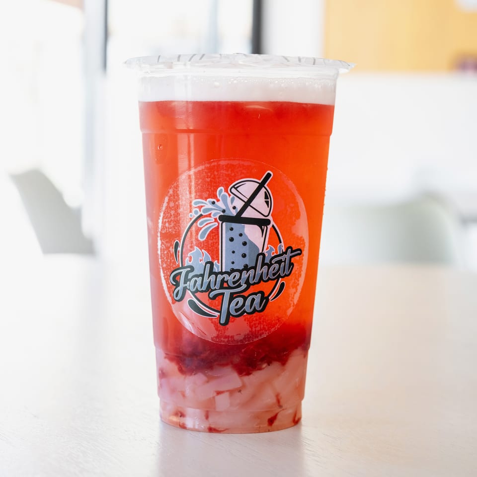 A Fahrenheit Tea strawberry drink with white jelly and a branded sticker on a light wooden table.
