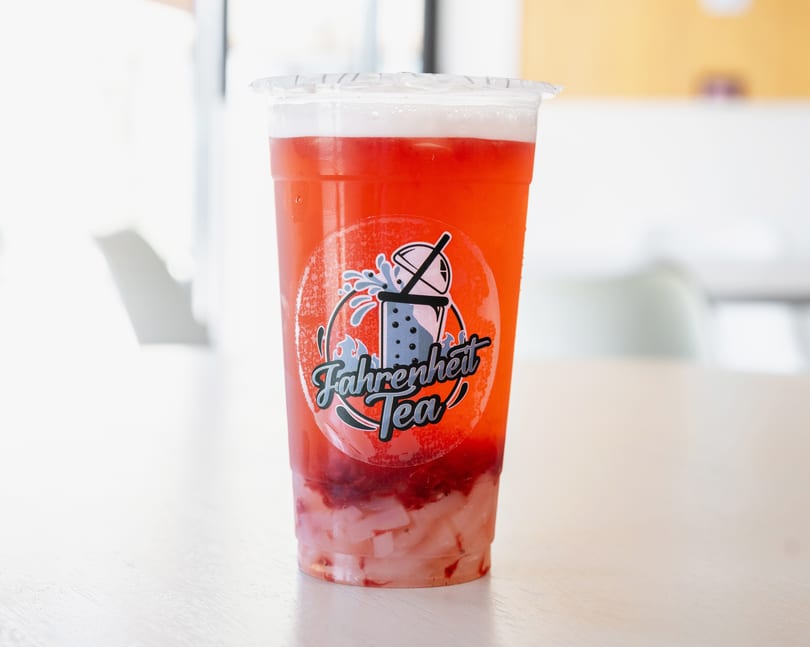 A Fahrenheit Tea strawberry drink with white jelly and a branded sticker on a light wooden table.
