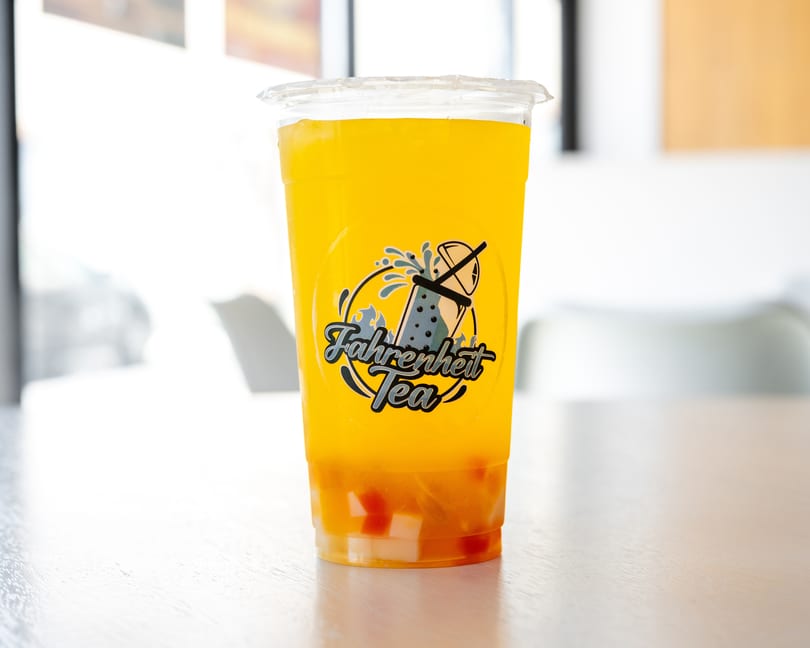 A Fahrenheit Tea drink, a vibrant yellow beverage with fruit pieces, sits on a light wooden table.