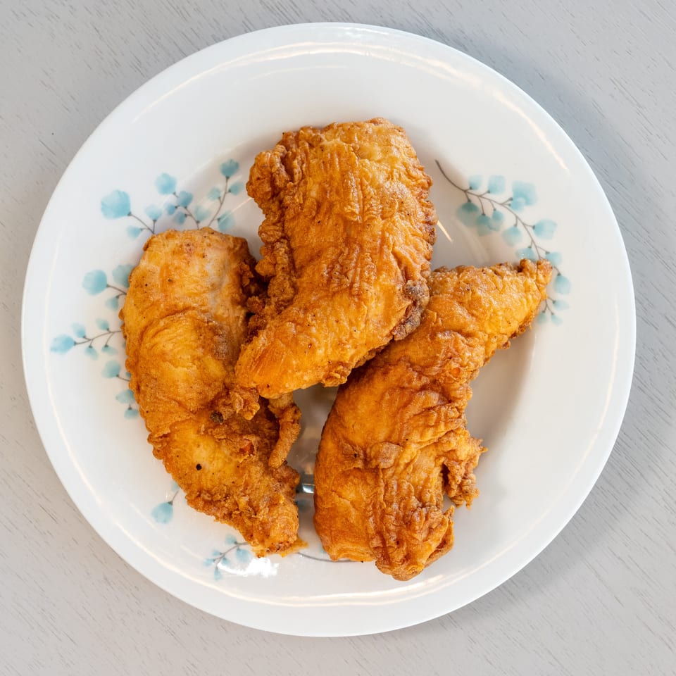 Three golden-brown fried chicken tenders are arranged on a white plate with blue floral designs.