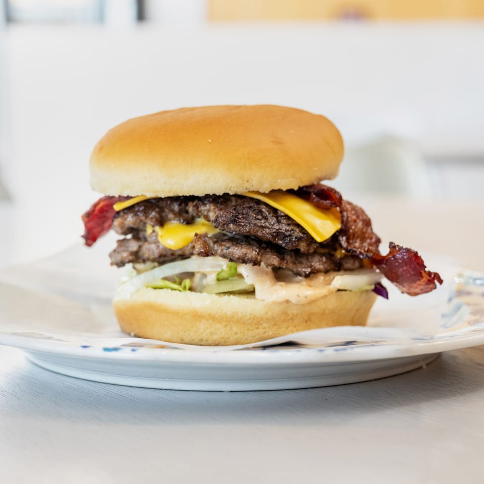 A double cheeseburger with bacon, lettuce, onions, and special sauce on a white plate.