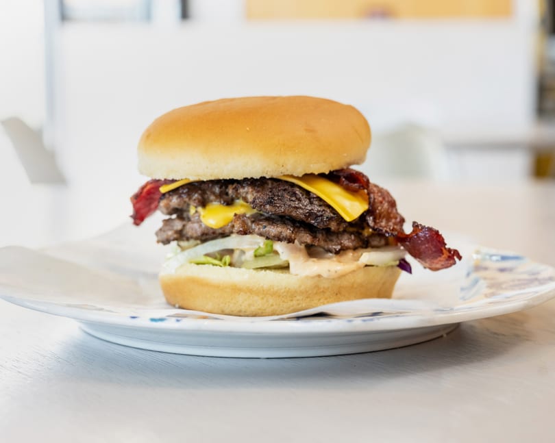 A double cheeseburger with bacon, lettuce, onions, and special sauce on a white plate.