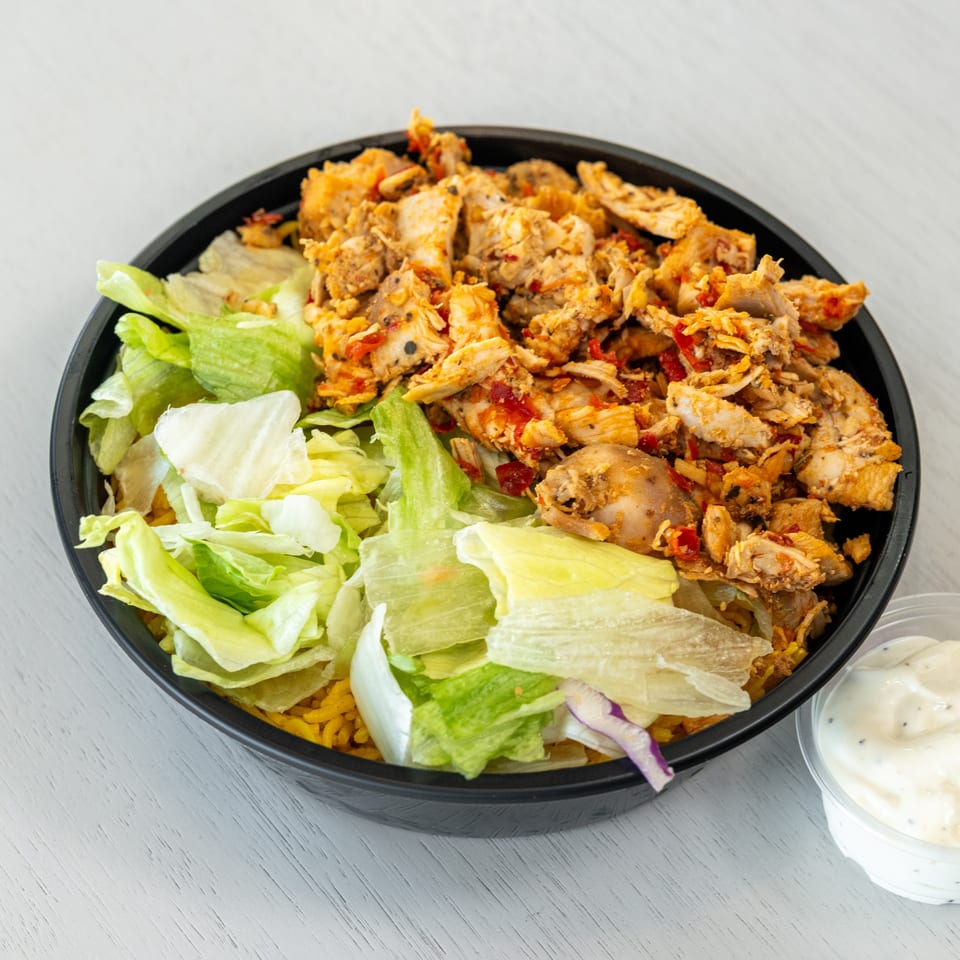 Chicken and rice bowl with lettuce and a side of white sauce on a white table.