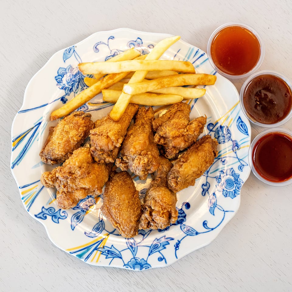 Crispy fried chicken wings and golden french fries on a decorative plate with three dipping sauces.